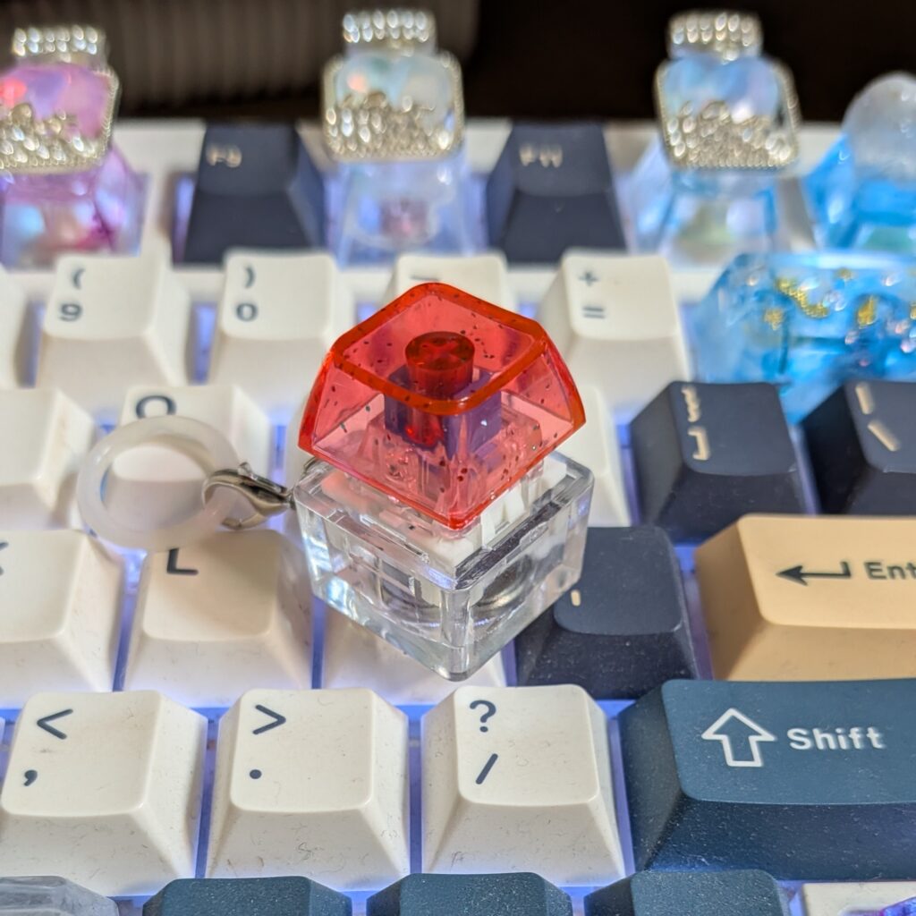 自作レジンキーキャップを装着したキーボードの上に置いた赤い透明キー型ガチャキーホルダー